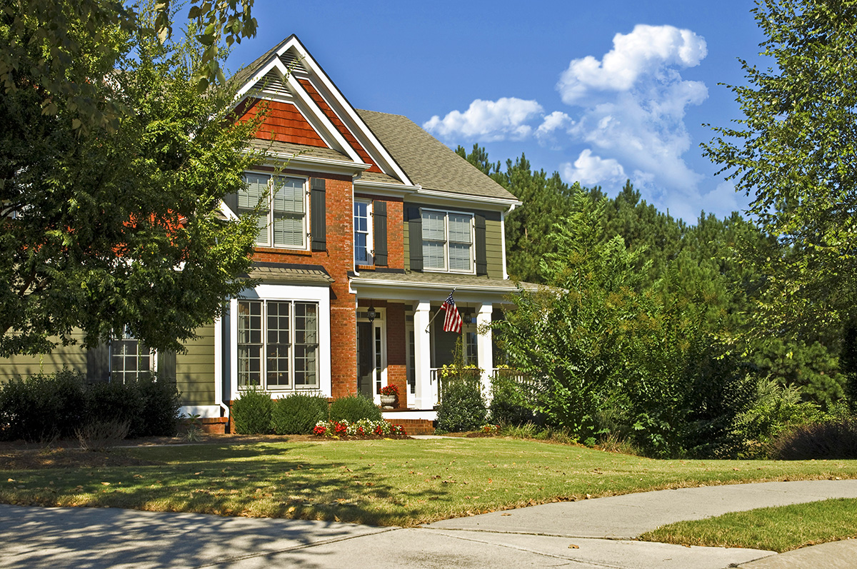 Exterior of a new, modern, red brick home showing the yard, driveway and sidewalk with mountain in the background. inspection services